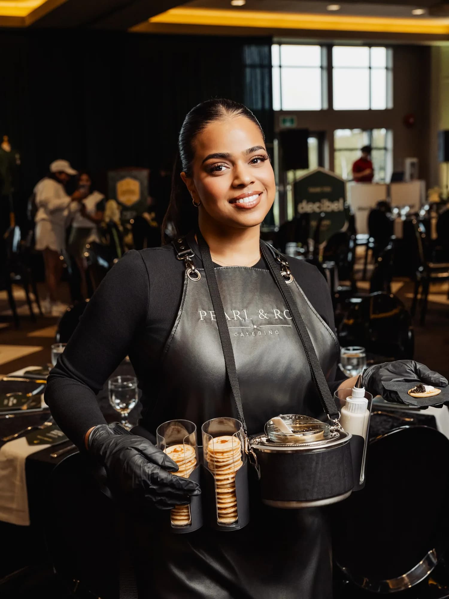 A smiling Pearl & Roe server holding blinis and a tin of caviar